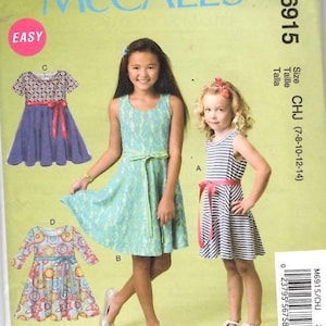 May include: McCall's M6915 sewing pattern envelope for children's dresses in sizes 7-14. The cover features illustrations of four sleeveless or short-sleeved dresses with waist ties, including floral, striped, and patterned designs on a light green background.
