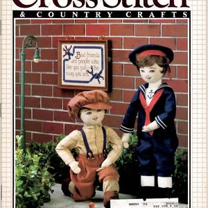 May include: The cover of a vintage "Cross Stitch & Country Crafts" magazine features two dolls. One doll kneels in overalls, and the other stands in a sailor suit. A framed cross-stitch quote reads, "Best friends are people who like you just the way you are."