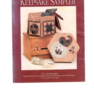May include: A book cover titled "Dream Spinners KEEPSAKE SAMPLER" featuring a patchwork project. The image shows a wooden box with pockets, a hexagonal box with a heart design, and a small wooden chest with drawers. The text reads "Pattern and directions for hexagonal box, patchwork pockets, and crazy quilt heart."