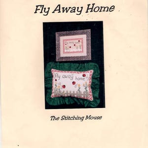 May include: A craft pattern titled "Fly Away Home" featuring cross-stitch designs. The image includes a framed piece and a pillow with ladybugs, flowers, and a picket fence. The text "The Stitching Mouse" is also visible.