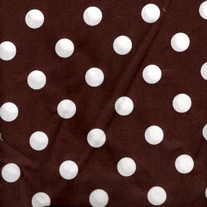 May include: Close-up of a brown fabric with a repeating pattern of large white polka dots. A wooden ruler with inch markings is at the bottom of the image. The fabric is likely used for sewing or crafting.