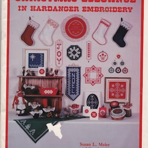 May include: A craft book titled Christmas Elegance in Hardanger Embroidery by Susan L. Meier and Rosalyn K. Watnemo. The cover displays various embroidered Christmas stockings, ornaments, wall hangings, and table linens in red, white, and blue.