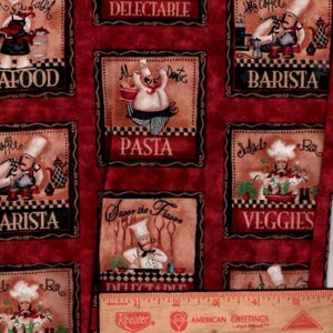 May include: A red fabric featuring a repeating pattern of rectangular panels with cartoon chefs and culinary text including DELECTABLE, PASTA, BARISTA, and VEGGIES. A wooden ruler is placed at the bottom, showing a length of 5.5 inches.