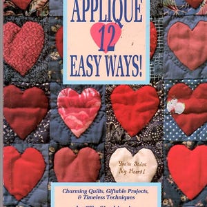 May include: A book cover featuring a patchwork quilt design with red heart appliqués on a blue background. The title "APPLIQUÉ 12 EASY WAYS!" is displayed prominently. The book is about charming quilts and giftable projects.