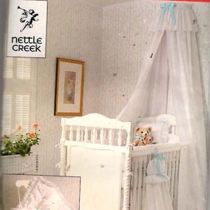 May include: A white baby crib with a canopy, adorned with light blue ribbons. The crib is decorated with a white skirt and a matching blanket. The image also features a teddy bear and the text "BUTTERICK" and "nettle CREEK".