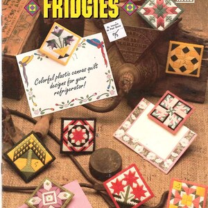 May include: A craft pattern booklet titled Quilt Block Fridgies by Annie's Attic featuring various square plastic canvas quilt designs. The cover displays multiple finished needlepoint projects with geometric and floral patterns in vibrant colors.