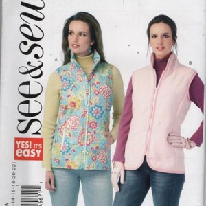 May include: A See & Sew B6081 sewing pattern envelope featuring two sleeveless vests. One vest is light blue with a multi-colored floral pattern, and the other is solid light pink. Both vests have a high collar, a front zipper, and rounded hems.