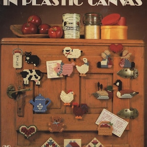 May include: A craft instruction booklet titled Magnets Go Country In Plastic Canvas by Anne Van Wagner Young. The cover displays various plastic canvas magnets including animals, hearts, and geometric shapes attached to a wooden cabinet surface.