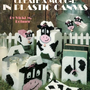 May include: A Leisure Arts craft leaflet titled Create a Moo-D in Plastic Canvas by Vicki M. Rohner. The cover features various plastic canvas projects with black and white cow patterns, including a tissue box cover, a carrier, and coasters.