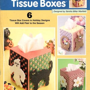 May include: A craft pattern booklet titled Holiday Tissue Boxes by The Needlecraft Shop featuring instructions for six plastic canvas tissue box covers. The cover displays various holiday-themed designs including a ghost, black cat, and flowers.
