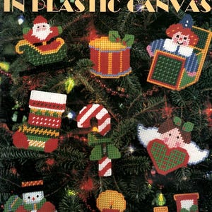 May include: A craft leaflet titled Looks Like Christmas in Plastic Canvas by Maryanne Moreck, featuring illustrations of a Santa in a sleigh, a drum, a jack-in-the-box, a stocking, a candy cane, an angel, a snowman, a candle, and a train.