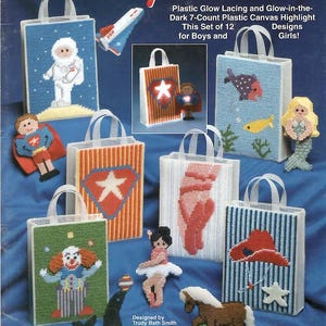 May include: A Needlecraft Shop plastic canvas pattern booklet titled Toys & Totes featuring 12 glow-in-the-dark designs. The cover displays various finished projects including tote bags with astronaut, superhero, clown, and nautical motifs.