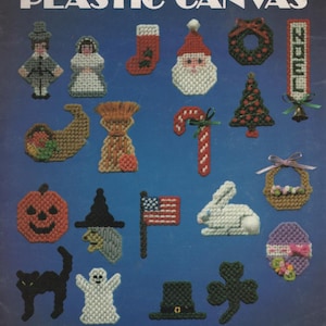 May include: A Leisure Arts craft leaflet titled Holiday Magnets for Plastic Canvas by Nancy Dorman. The blue cover displays 23 stitched holiday-themed designs including a Santa, pumpkin, ghost, black cat, American flag, and various seasonal icons.