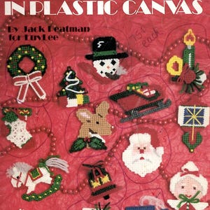 May include: A craft instruction booklet titled Yuletide Ornaments in Plastic Canvas by Jack Peatman for LuvLee. The red cover features illustrations of various holiday-themed plastic canvas ornaments including a wreath, snowman, sleigh, and train.