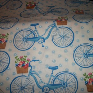 May include: A white fabric with a repeating pattern of blue bicycles with baskets of flowers. The bicycles have white tires and are on a white background with a blue snowflake pattern.