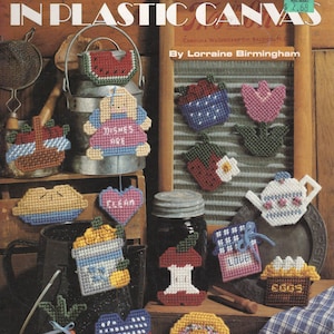 May include: A craft instruction booklet titled Cute & Country Magnets IN PLASTIC CANVAS by Lorraine Birmingham, featuring various plastic canvas magnets including a watermelon, a doll, a teapot, an apple core, and a basket of vegetables.