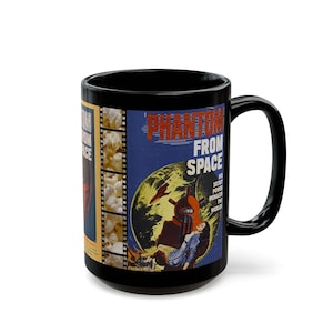 May include: A black ceramic mug featuring a vintage movie poster graphic for Phantom From Space. The design includes a film strip border filled with popcorn, a blue background, and text that reads Phantom From Space His Secret Power Menaced The World.