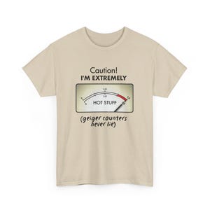May include: A beige t-shirt with the text "Caution! I'm Extremely Hot Stuff" above a graphic of a gauge. The gauge reads high, and the text "(geiger counters never lie)" is below the gauge.