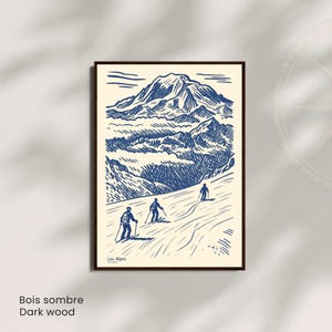 May include: A framed print with a blue and white illustration of a mountain range and skiers. The artwork includes the text "Les Alpes" and "Dark wood". The print is in a dark wood frame.