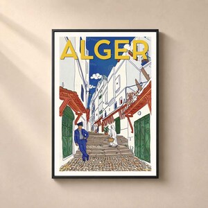 May include: A framed travel poster featuring a street scene in Algiers with the word ALGER in large yellow letters at the top. The illustration shows white buildings, a stone staircase, a person in a blue suit, and a person in a white robe.