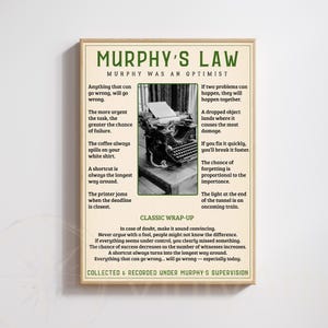 May include: A framed print with the title "Murphy's Law" in a vintage style. The print features a list of humorous observations and a black and white image of a typewriter. The text is in a serif font.