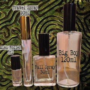 May include: Four clear glass fragrance bottles of varying sizes. From left to right: a 5ml Mini Roller with a black cap, a 10ml Travel Spray with a gold cap, a 30ml Full Spray with a black cap, and a 120ml Big Boy spray bottle with a black cap.