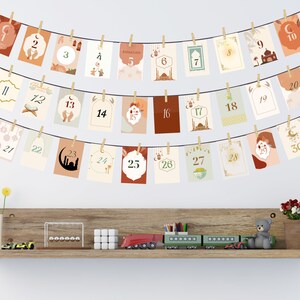 May include: A string of 30 cards with gold numbers and Islamic-themed illustrations, hanging on a white wall. The cards are decorated with crescent moons, stars, lanterns, and mosques. The cards are numbered 1 through 30, with the word "Ramadan" on the fifth card.