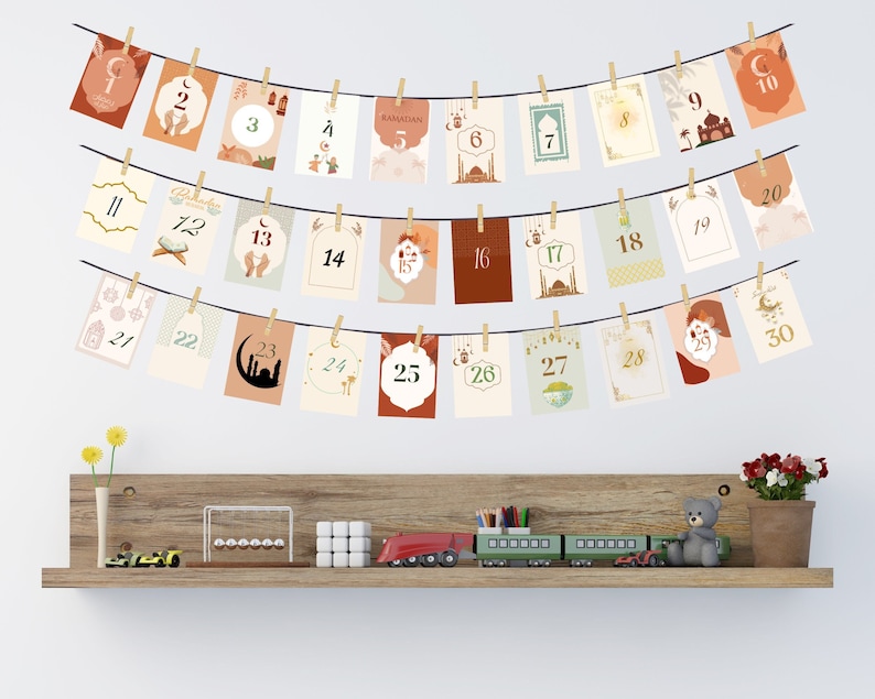 May include: A Ramadan countdown calendar with 30 cards featuring different Islamic designs and numbers from 1 to 30. The cards are strung together with twine and clothespins.