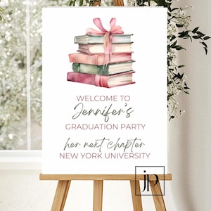 Könnte beinhalten: Ein weißes Schild mit einem rosa Band und einem Stapel Bücher. Auf dem Schild steht "Willkommen zur Abschlussparty von Jennifer ihr nächstes Kapitel NEW YORK UNIVERSITY".