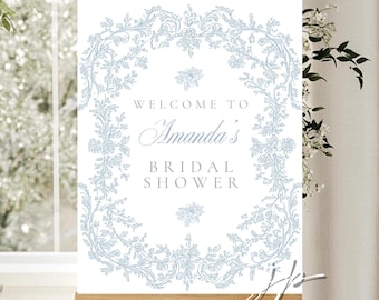 May include: A white sign on a wooden easel with the text "Welcome to Amanda's Bridal Shower." The text is in a light blue script font, surrounded by a light blue floral wreath design.
