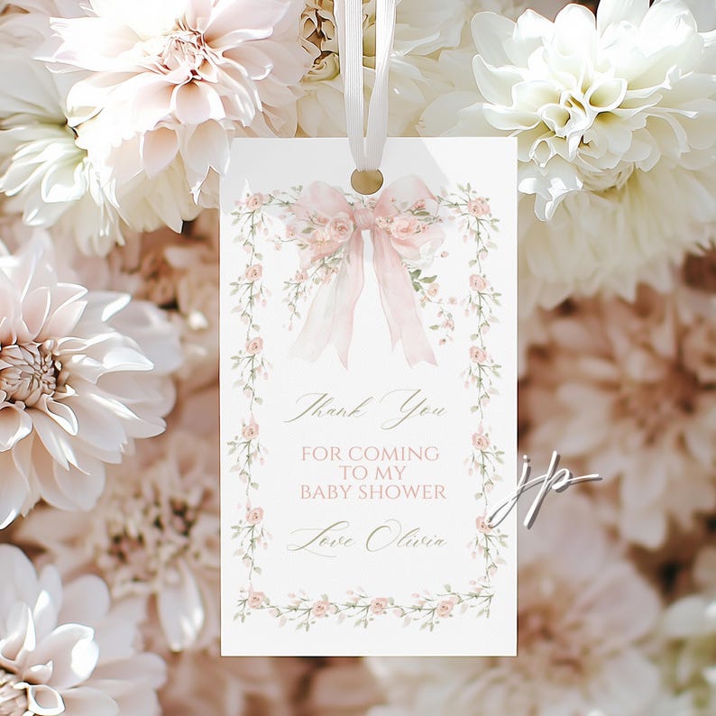 May include: A baby shower thank you tag with a pink bow and floral border. The tag reads "Thank You for Coming to My Baby Shower Love Olivia". The tag is hanging from a white ribbon.