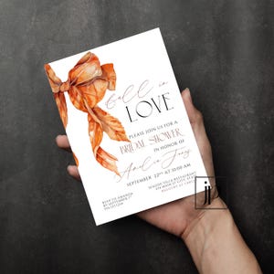 May include: A white rectangular invitation card featuring a watercolor illustration of a large orange ribbon bow on the left side. The text reads Fall in LOVE, PLEASE JOIN US FOR A BRIDAL SHOWER IN HONOR OF Amelia Jones, SEPTEMBER 22ND AT 10:00 AM.