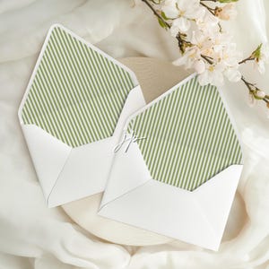 Peut inclure: Deux enveloppes blanches avec une doublure à rayures vertes et blanches. Les enveloppes sont ouvertes, révélant le motif à rayures. Une branche de fleurs blanches est en arrière-plan. Les enveloppes sont sur une surface blanche.
