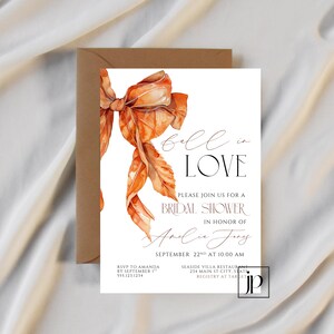 May include: A white bridal shower invitation card featuring a large watercolor orange bow. The text reads: fall in LOVE, PLEASE JOIN US FOR A BRIDAL SHOWER IN HONOR OF Amelia Jones, SEPTEMBER 22ND AT 10:00 AM, RSVP TO AMANDA BY SEPTEMBER 1ST 555.123.1234, SEASIDE VILLA RESTAURANT 234 MAIN ST CITY, STATE, REGISTRY AT TARGET.