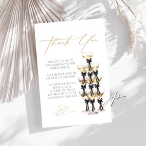 May include: A white card with gold calligraphy reading "Thank You." The card features a champagne tower illustration with black bows. Text on the card expresses gratitude for a 50th birthday celebration.