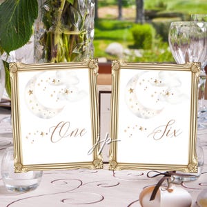 May include: Two framed table number cards with gold frames. Each card features a watercolor design of a crescent moon, clouds, and stars. One card reads "One" and the other reads "Six".