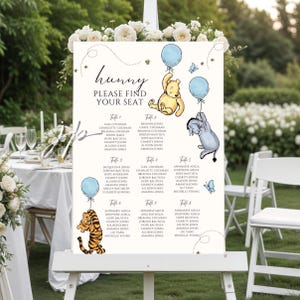 May include: A white easel sign with the text "hunny PLEASE FIND YOUR SEAT" and illustrations of Winnie the Pooh characters. The sign lists names under table numbers, with blue balloons and butterflies.