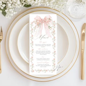 May include: A vertical rectangular menu card featuring a soft pink watercolor bow at the top and a floral vine border. The text reads Menu, the apps, Coconut Cashew Chicken, the entrees, Grilled Lemon Chicken, Pasta Primavera, and Sweet Endings.