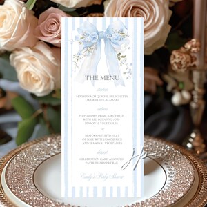 Puede incluir: Tarjeta de menú para baby shower con lazo azul claro y detalles florales. El menú incluye entrantes, platos principales y postres. El texto dice "Emily's Baby Shower."