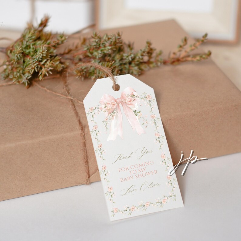May include: A gift tag with a pink bow and floral accents, tied to a wrapped package. The tag reads "Thank You for coming to my baby shower Love Olivia."