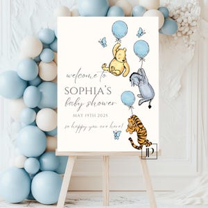 May include: A Winnie the Pooh themed baby shower welcome sign with blue and yellow balloons, butterflies, and the text "Welcome to Sophia's Baby Shower May 19th 2025 So happy you are here!"