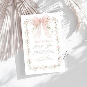 May include: A baby shower thank you card featuring a pink bow and floral wreath. The card says "BABY SHOWER Thank You" with a message of gratitude and names "Elizabeth & Brian". The card is white with a soft, elegant design, perfect for a baby shower.