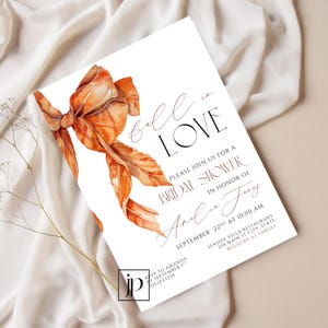 May include: A white bridal shower invitation card featuring a watercolor illustration of a large, burnt orange ribbon bow. The text reads: fall in LOVE, PLEASE JOIN US FOR A BRIDAL SHOWER IN HONOR OF Amelia Jones, SEPTEMBER 22ND AT 10:00 AM.