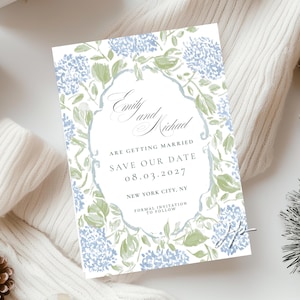 May include: A wedding invitation with a floral design. The invitation features the names "Emily and Michael" in elegant script, along with the text "Save Our Date 08.03.2027, New York City, NY". The design includes blue and green watercolor floral elements.