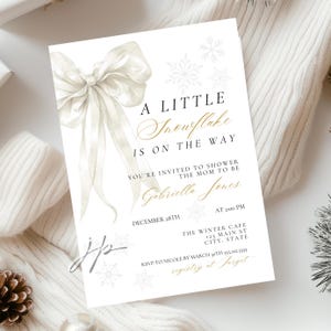 May include: Baby shower invitation in white with a watercolour bow and snowflake design. The text reads "A Little Snowflake Is On The Way" with event details, including the date, time, and location.