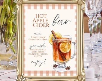 Puede incluir: Un letrero rectangular en un marco dorado ornamentado con el texto Hot Apple Cider Bar, una receta para mezclar y decorar, y una ilustración de una taza de cristal llena de sidra, rodajas de naranja y una rama de canela sobre un fondo a cuadros.