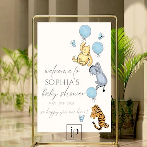 May include: A Winnie the Pooh themed baby shower welcome sign with blue and white balloons, butterflies, and the text "Welcome to Sophia's Baby Shower May 19th 2025 So happy you are here!"