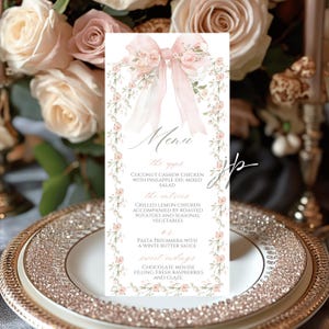 Könnte beinhalten: Eine Hochzeitsmenükarte mit floralem Design. Das Menü zeigt oben eine rosa Schleife und einen floralen Rand. Das Menü umfasst Vorspeisen, Hauptgerichte und Desserts. Die Karte befindet sich auf einem dekorativen Teller.