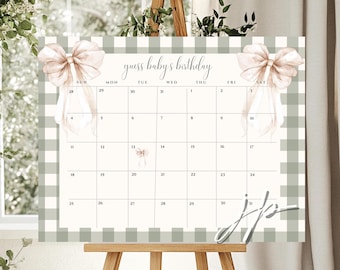 May include: A baby shower calendar with a green and white gingham border. The calendar features the text "guess baby's birthday" and is decorated with watercolor bows. The calendar is displayed on a wooden easel.