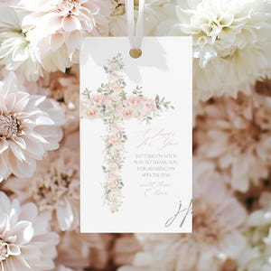 Op de afbeelding: Een witte bedanklabel met een bloemen kruisontwerp. Het kruis is gemaakt van roze en witte rozen en groen. Het label heeft een gouden oogje en een wit lint. De tekst luidt "A Favor For You" en een bericht.